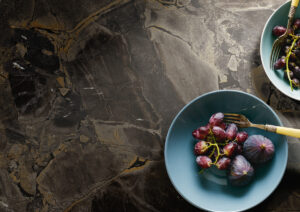 Figs and black grapes in blue bowls on marble surface.